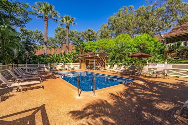 Sunny shared pool area features lounge seating and tropical landscaping