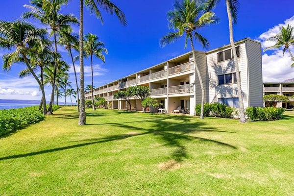 Resort building overlooks expansive lawn, palm trees, and coastal surroundings