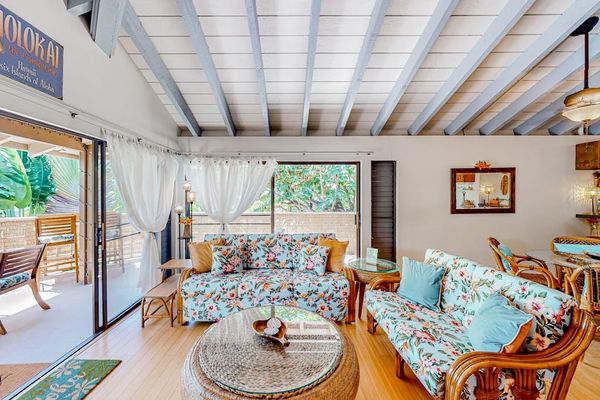 Living room features patterned seating, coffee table, artwork, and windows