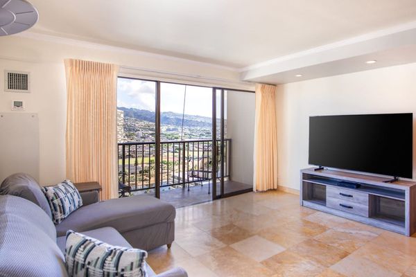 Bright open-concept living room with a private balcony, Smart TV, and panoramic city and mountain views.