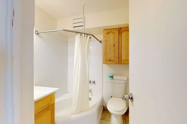The full bathroom provides a clean and functional space, featuring a standard shower and tub combination, neutral tile flooring, and a convenient wall-mounted wooden cabinet for extra storage.