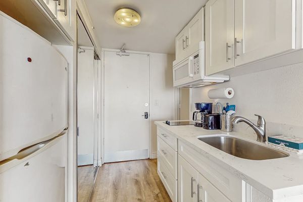 Bright white cabinets and a stainless steel sink complete the entrance corridor, offering practical storage for extended stays.