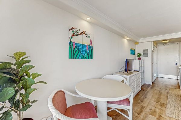 The entryway features a cozy seating spot, tropical artwork, and sleek wood-style flooring.