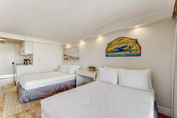A welcoming sleeping area is outfitted with two full sized beds, ambient lighting, and tropical wall decor.