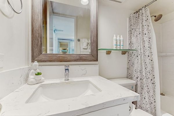 The full bathroom includes a modern vanity with a quartz-style countertop, a large framed mirror, and convenient shelving.
