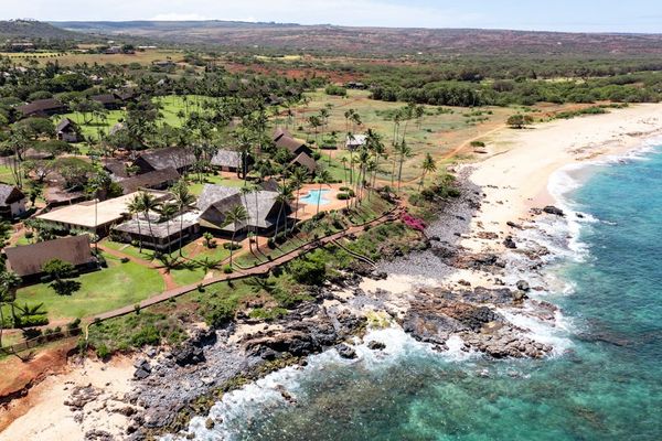 Aerial coastline showcases resort homes, rocky shore, ocean, and hills