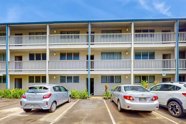 Resort building displays balconies, palm landscaping, parking spaces, and skies