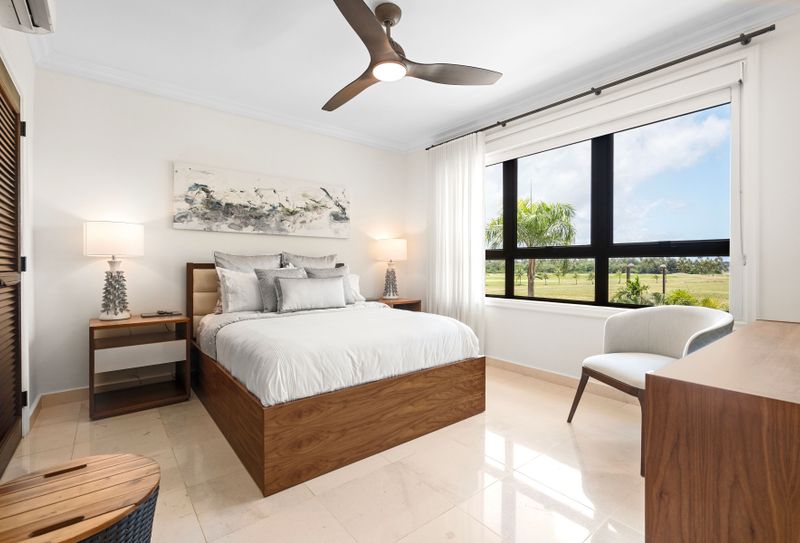 This tranquil bedroom is the perfect escape. The plush bed, wrapped in soft linens, and the neutral colors create a calming vibe. Large windows let in lots of natural light, offering beautiful views of the lush greenery and golf course. A cozy armchair makes a great reading nook, while a sleek nightstand and stylish lamp add the finishing touches to this inviting space.