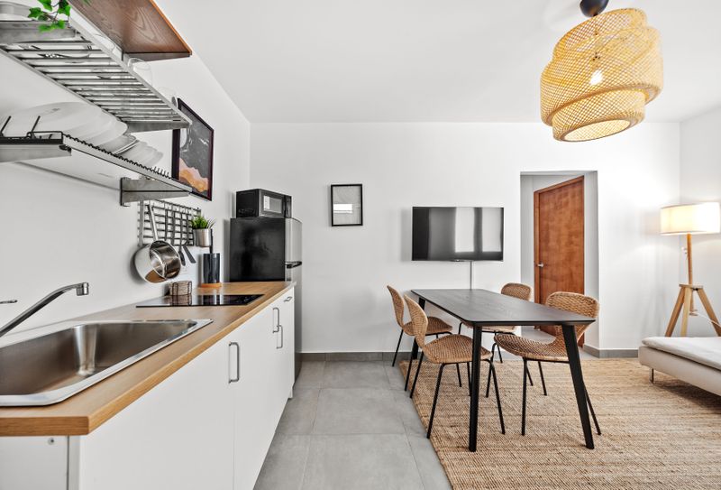 Enjoy a seamless experience of cooking, dining, and relaxing in this spacious kitchen area, featuring sleek appliances, a cozy dining table, and a flat-screen TV.