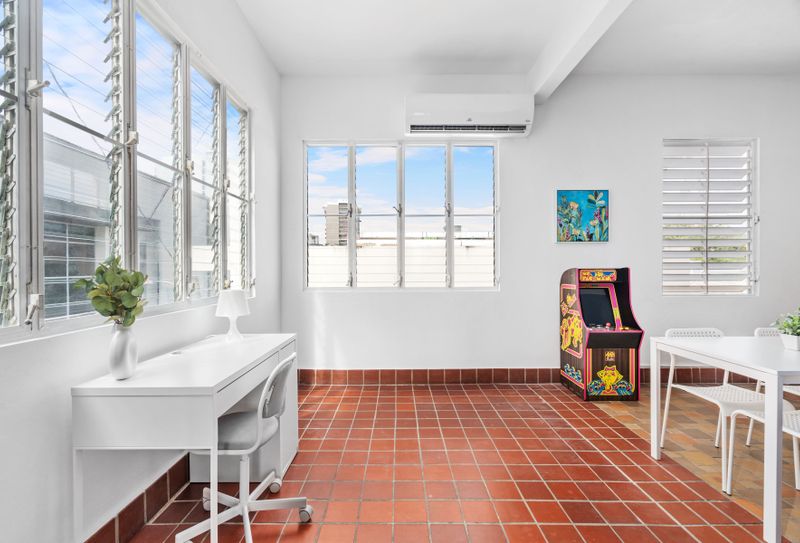 A spacious living room with airconditioner, desk and seat, dining table, large windows and pacman arcade came