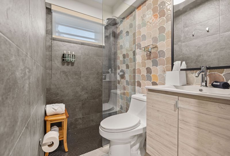 A modern bathroom with sleek grey tile walls, a single vanity with a vessel sink, and plush white bathrobes hanging invitingly on hooks