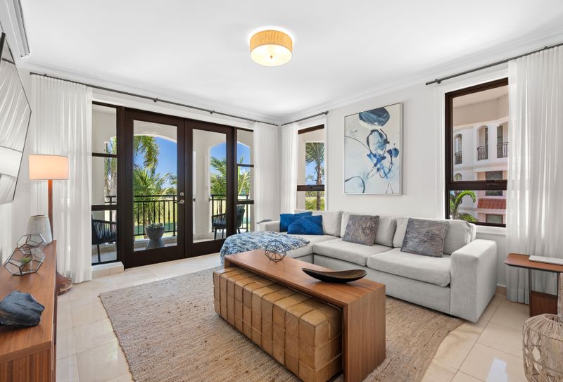 This inviting living space boasts a chic and modern design, with a comfortable L-shaped sofa, a stylish coffee table, and a large flat-screen TV. The room is bathed in natural light from the sliding glass doors that lead out to a spacious balcony, offering stunning views of the pool and lush tropical surroundings.