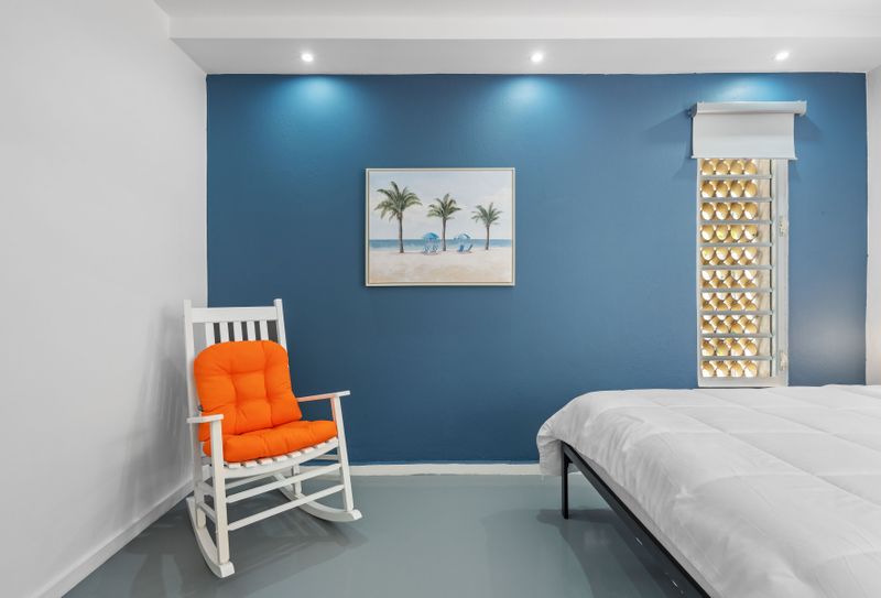 Enjoy a cozy, modern room with a bold blue accent wall, comfortable white rocking chairs, and contemporary decor, creating a vibrant yet relaxing space.