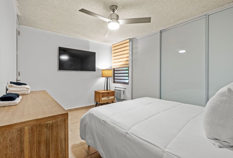 This modern bedroom is designed for relaxation, featuring a large bed with plush pillows and a convenient, sleek media setup for entertainment.