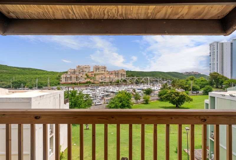Wake up to this breathtaking view from your balcony, showcasing a sprawling marina bordered by lush green hills and modern architecture.