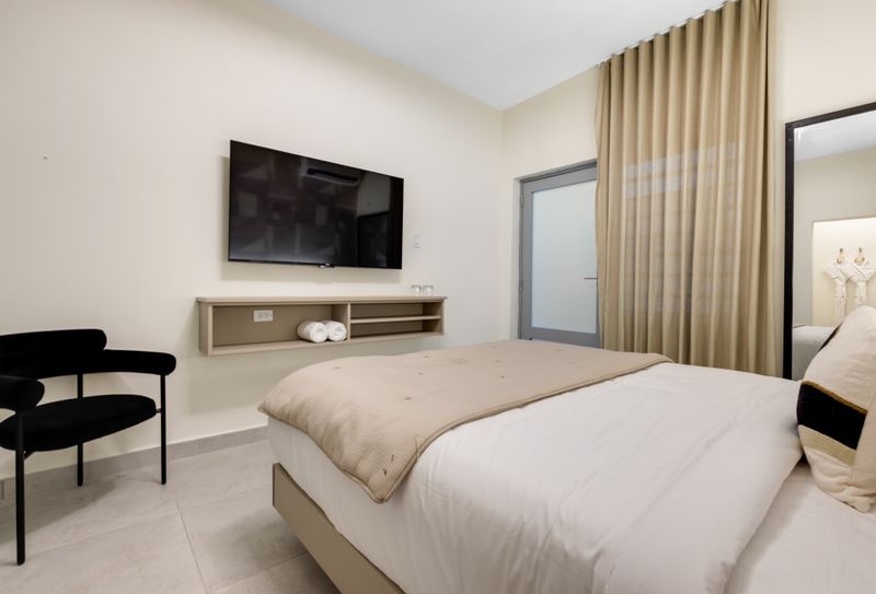 A modern bedroom with a sleek TV mounted on the wall, a large mirror, and a comfortable bed with plush pillows.