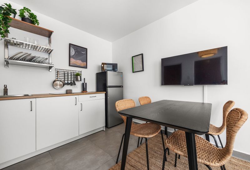 Prepare meals, enjoy your meals, and unwind in this well-equipped kitchen area, complete with modern appliances, a dining table, and a TV.
