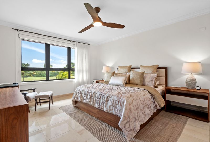 This cozy bedroom is all about relaxation and style. The king-sized bed with its soft linens and neutral headboard is super comfy. Big windows let in lots of natural light and offer great views of the golf course. A modern ceiling fan and air conditioning keep it cool, and the sleek nightstand and lamp add a nice touch
