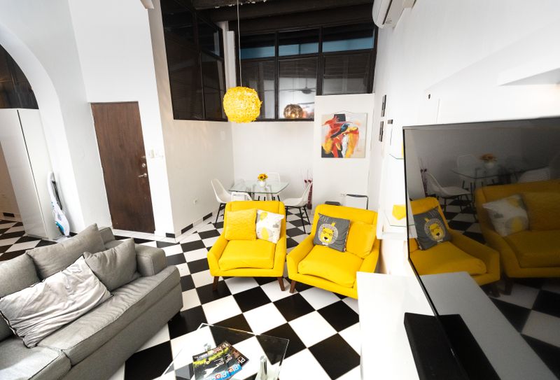 Experience vibrant comfort in this inviting living room. With a large grey sofa, cheerful yellow cushions, and two additional seats, there's ample space for everyone to gather. Enjoy entertainment on the smart TV in this lively and welcoming space.