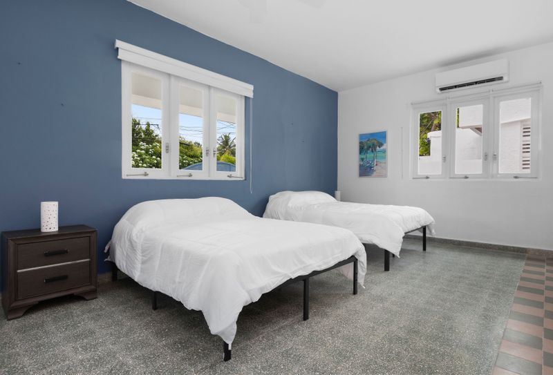 Bright bedroom featuring two single beds with stylish bedding. There’s a small nightstand between the beds and a window that lets in natural light, making the room feel airy and open.