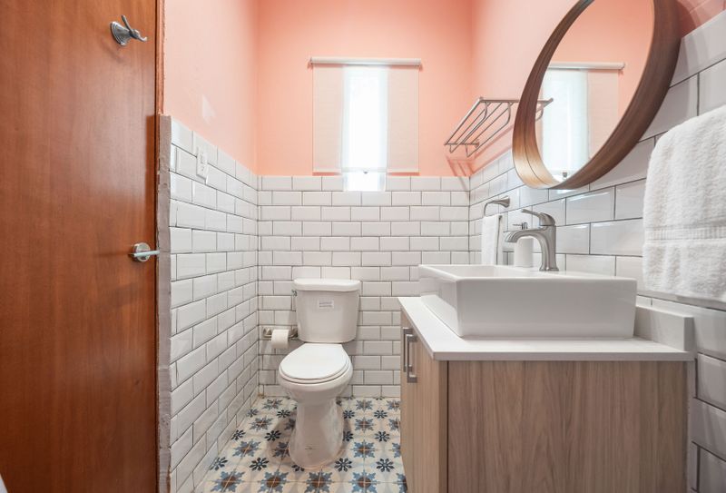 Modern bathroom, with mirror and cabinets, comfortable toilet . where classic design meets modern comfort. The soft peach walls create a warm and inviting ambiance, beautifully complemented by the crisp white subway tile and playful patterned floor.
