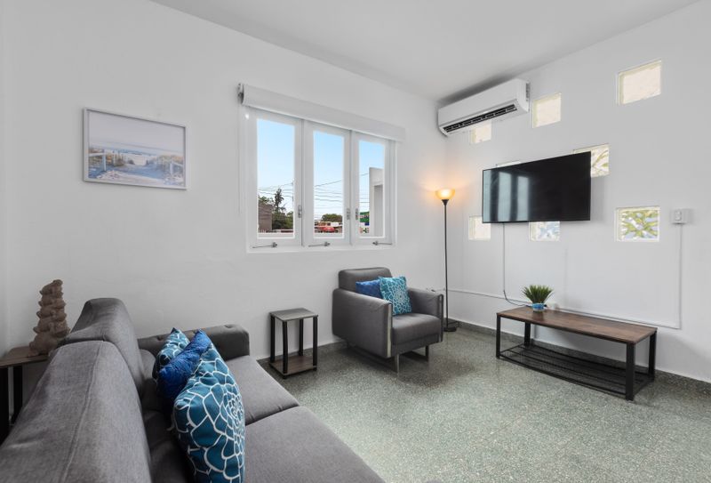 Spacious living room with two large, comfortable sofas, perfect for relaxing. A smart TV is mounted on the wall, and a collection of board games is available on the shelf for entertainment. The room has plenty of natural light from large windows.