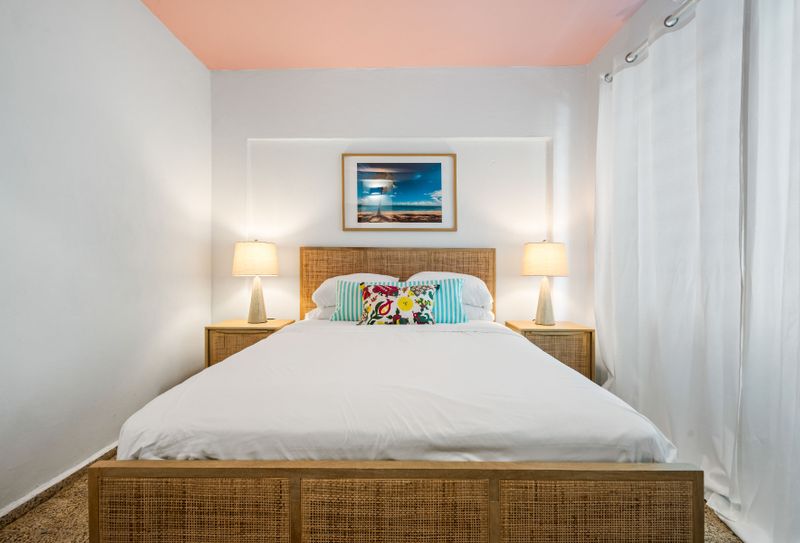 Dreamy Tropical Retreat: Unwind in our inviting bedroom featuring a comfortable bed with a stylish rattan headboard, flanked by warm, ambient lighting. The vibrant wall art adds a touch of paradise.