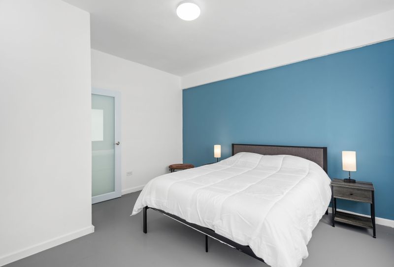 A serene space boasting a plush bed, minimalist decor, and a vibrant blue accent wall that adds a touch of warmth and sophistication.