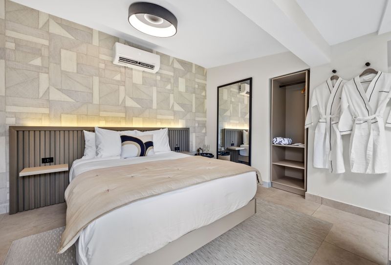Modern and minimalist bedroom featuring a large, comfortable bed with crisp white linens and plush pillows, accented by a stylish beige headboard.