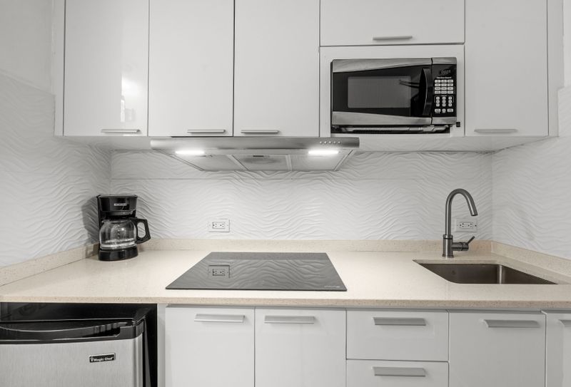 Whip up delicious meals in your fully equipped, modern kitchen featuring sleek white cabinetry, a microwave, and a convenient cooktop. Perfect for preparing your morning coffee or a gourmet dinner!
