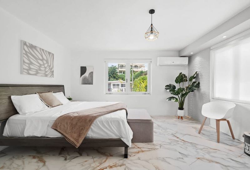 bright bedroom wiht king sized bed, lounge chair, wall art, ceiling lamp and windows and white curtains and air conditioner