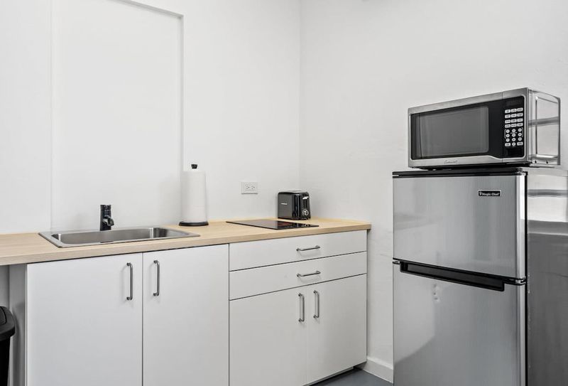 Delight in the practical elegance of this fully equipped kitchenette, featuring sleek stainless steel appliances, a warm wooden countertop, and crisp white cabinetry.