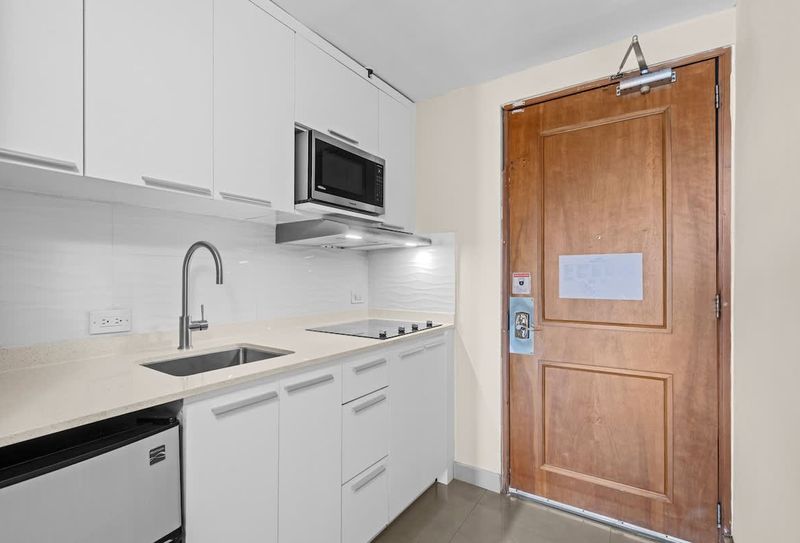 Step into your bright and inviting studio apartment, featuring a modern kitchen equipped for all your culinary needs. Notice the handy fire extinguisher for peace of mind, ensuring a safe and comfortable stay.