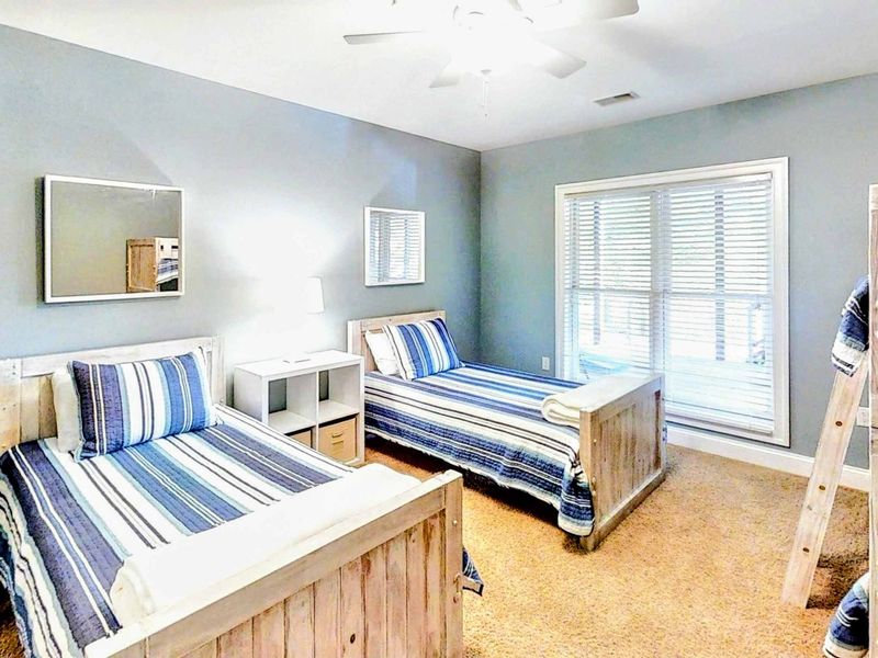 This spacious and inviting bunk room is perfect for families or groups, featuring two twin beds, a twin-over-twin bunk, cozy coastal decor, and plenty of natural light.