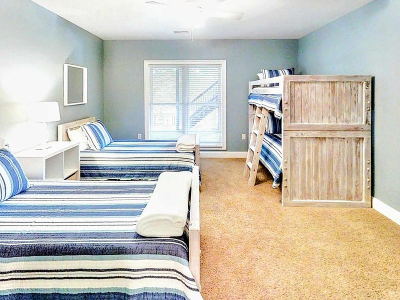 This spacious and inviting bunk room is perfect for families or groups, featuring two twin beds, a twin-over-twin bunk, cozy coastal decor, and plenty of natural light.
