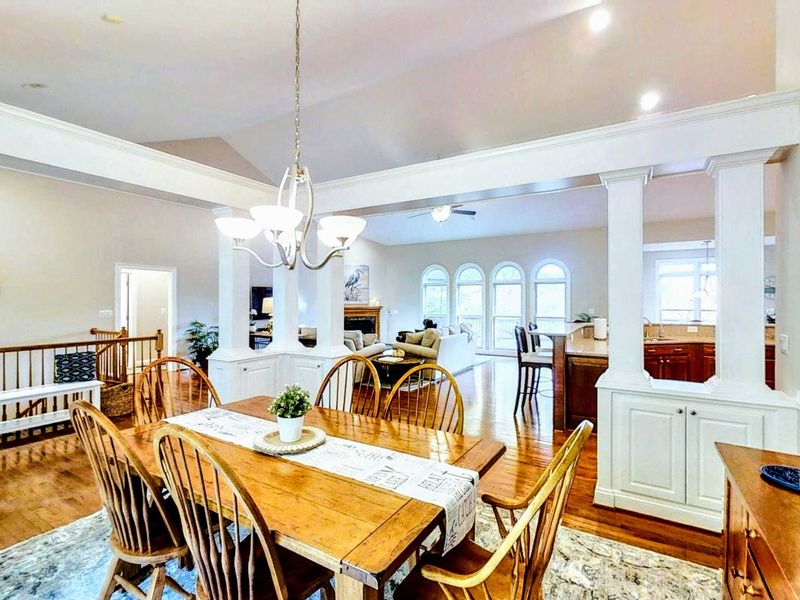 Gather around the elegant farmhouse-style dining table in this beautifully lit space, featuring warm wood tones, stylish decor, and an open-concept design perfect for memorable meals.