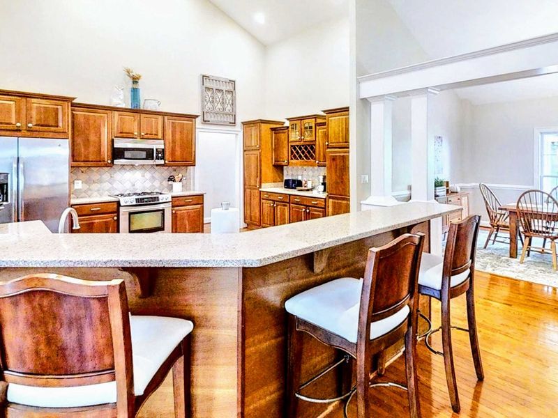 This spacious kitchen features rich wood cabinetry, modern stainless steel appliances, and a large wraparound breakfast bar perfect for morning coffee or evening conversations.