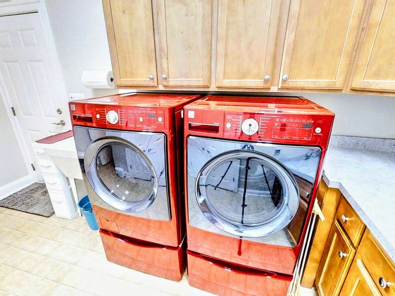 Enjoy the convenience of a fully equipped laundry room featuring modern red washer and dryer units, ample counter space, and plenty of storage.