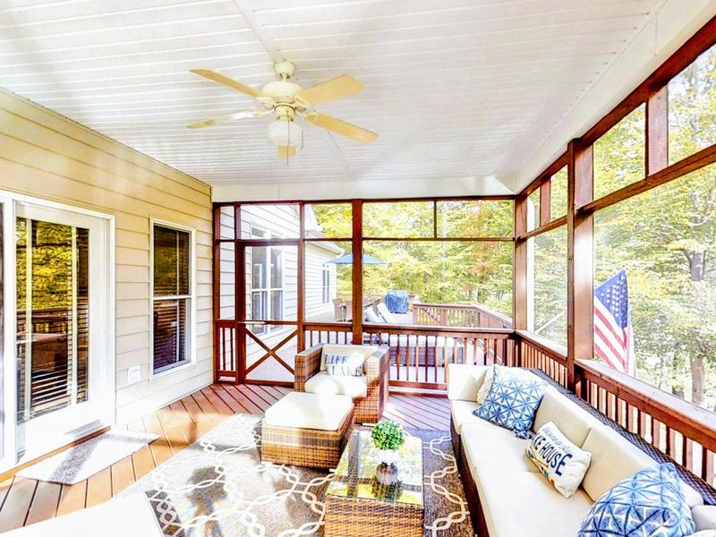 Relax in the comfort of this beautiful screened-in porch, featuring cozy seating, a ceiling fan, and peaceful views of the surrounding trees and lake.