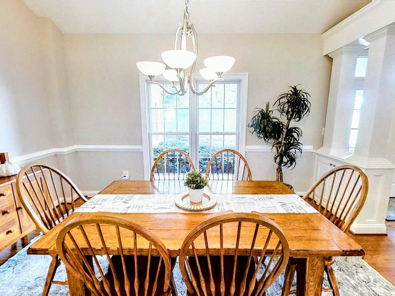 Gather around the elegant farmhouse-style dining table in this beautifully lit space, featuring warm wood tones, stylish decor, and an open-concept design perfect for memorable meals.