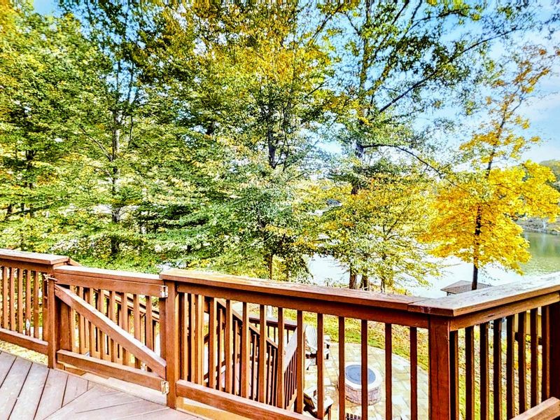 Step out onto this beautiful wooden deck with gated access, offering a peaceful overlook of the lush trees, fire pit area, and serene lake views below.