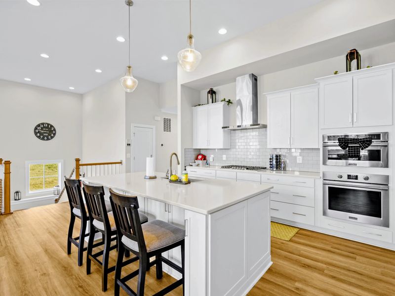 Kitchen - Three-stool island with gas cooktop, steel hood, and double ovens visible along the prep wall.