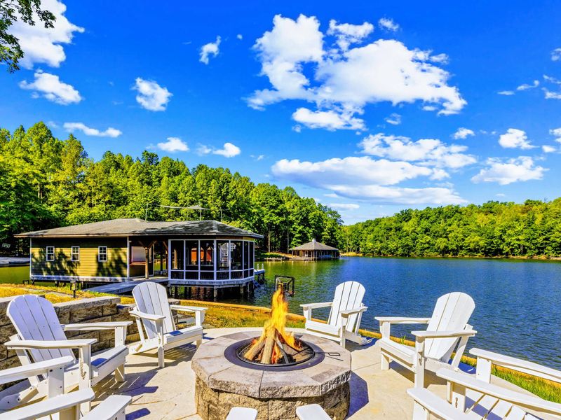 Fire Pit - A stone fire pit ringed with white Adirondack chairs at the water's edge, the boathouse and lake glowing just beyond.