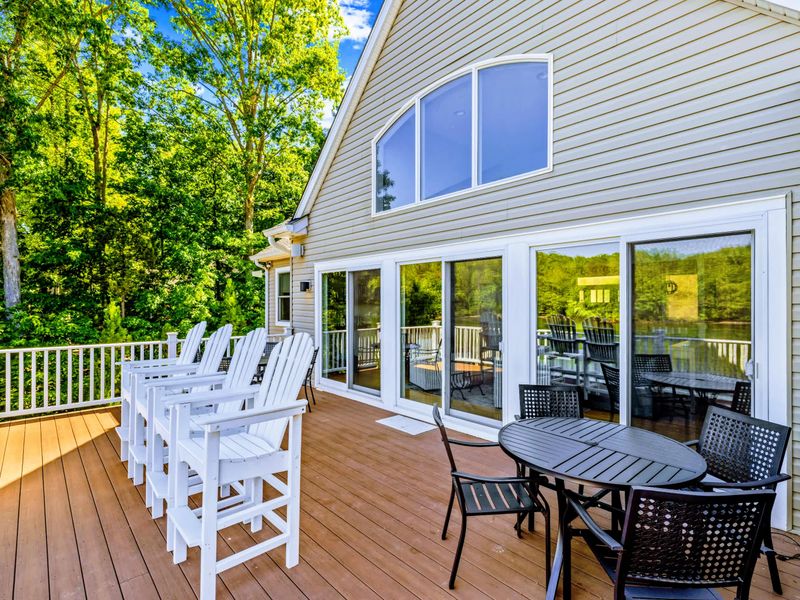Upper Deck - White Adirondack chairs and a dining table on the spacious deck, the screened porch and lake just beyond.
