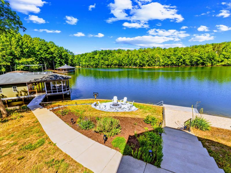 Aerial View - Looking down over the fire pit patio, landscaped lawn, and the dock reaching out into the quiet cove.