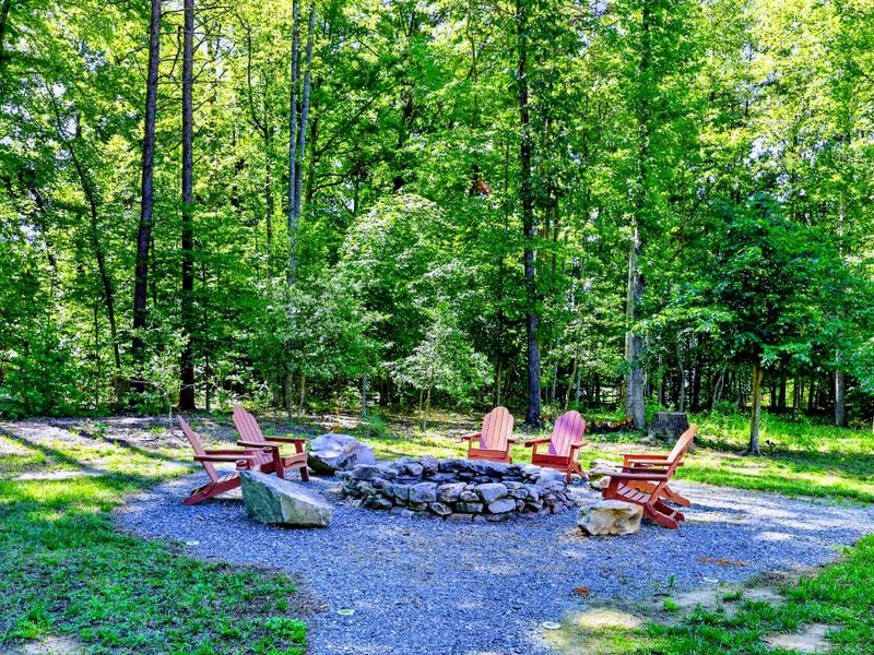 Fire Pit - Adirondack chairs circle the stone fire pit in a clearing ringed by tall pines.