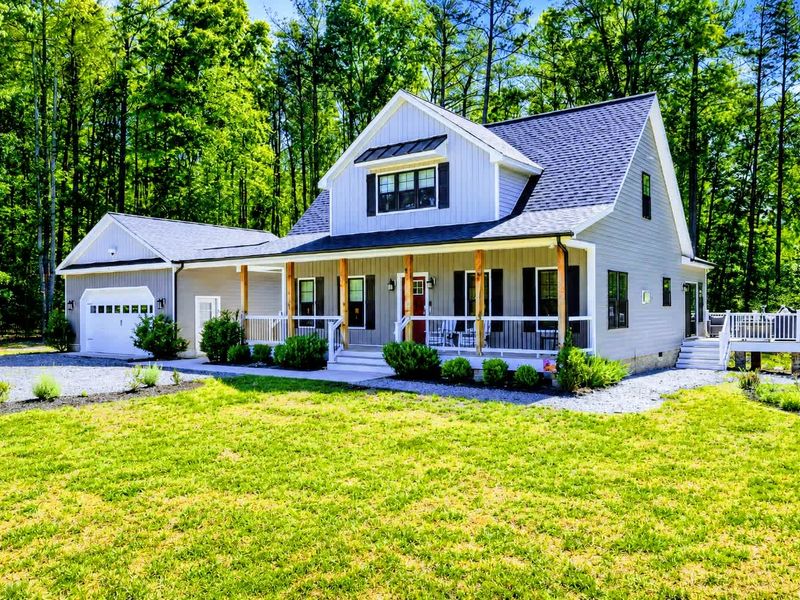 Exterior - Gray craftsman home with a wraparound porch, manicured lawn, and two-car garage on a private wooded lot.