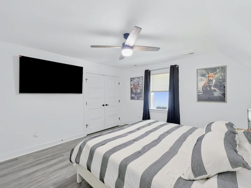 Bedroom - King bed with gray striped bedding, wall-mounted TV, and nature prints in a bright, airy room.