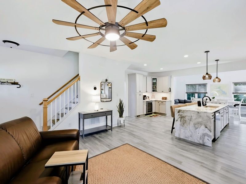 Living Room - Wide open-concept view flowing into the kitchen and dining, with a statement windmill fan overhead.
