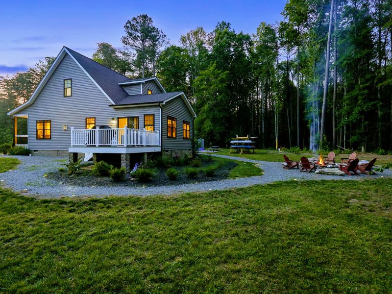 Deck - The home's multi-level deck and fire-pit yard glow at twilight against the wooded backdrop.